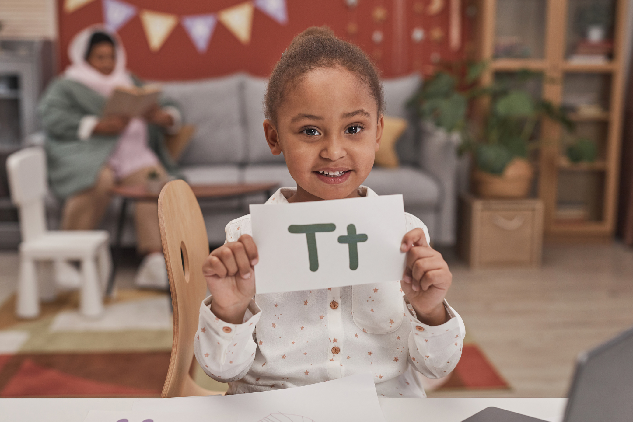Close-Up Shot of a Girl Holding an Alphabet Card while Looking at Camera